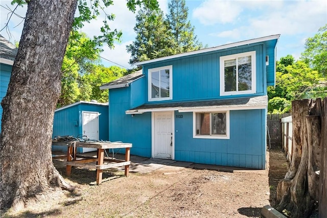 rear view of property featuring an outdoor structure, fence, roof with shingles, a patio area, and a storage shed