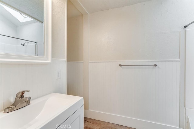 bathroom with a skylight, a shower, wood finished floors, a wainscoted wall, and vanity