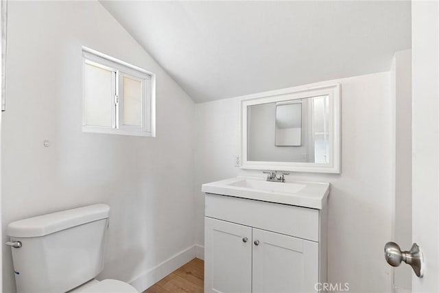 bathroom with vanity, toilet, baseboards, wood finished floors, and vaulted ceiling
