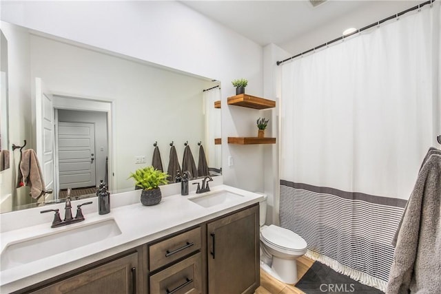 bathroom featuring double vanity, toilet, a sink, and wood finished floors