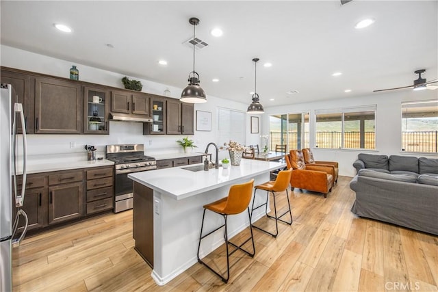 kitchen with dark brown cabinets, appliances with stainless steel finishes, a sink, a breakfast bar area, and under cabinet range hood