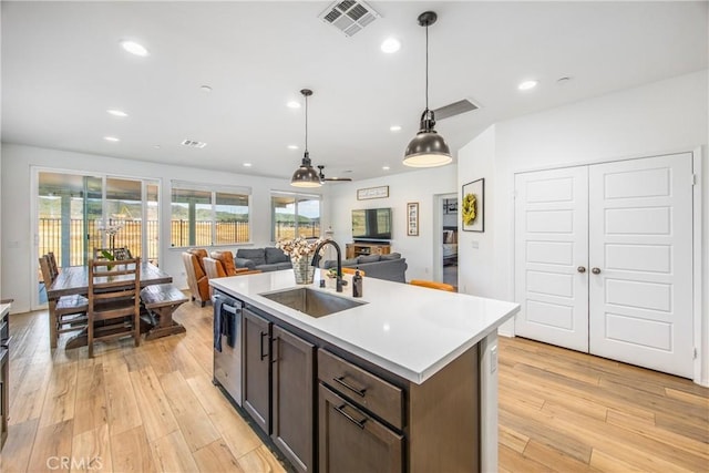 kitchen with visible vents, dark brown cabinets, open floor plan, light countertops, and a sink