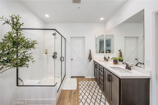 full bathroom featuring visible vents, a sink, wood finished floors, and a shower stall