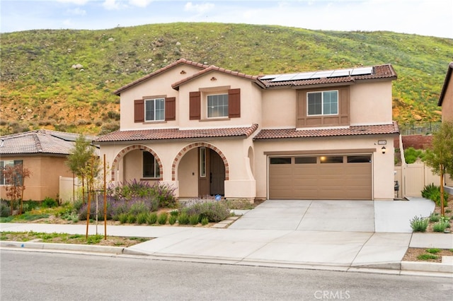 mediterranean / spanish-style home featuring a garage, covered porch, roof mounted solar panels, driveway, and a tile roof