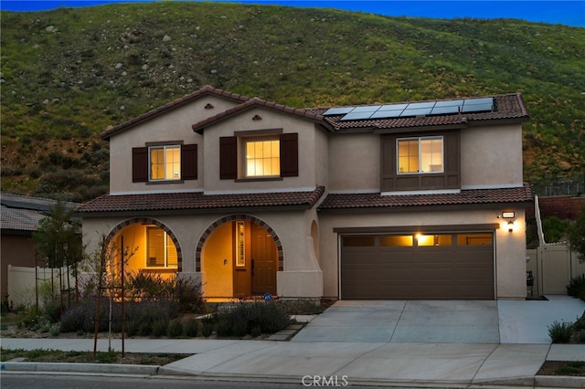 mediterranean / spanish-style home featuring a garage, stucco siding, concrete driveway, a porch, and solar panels