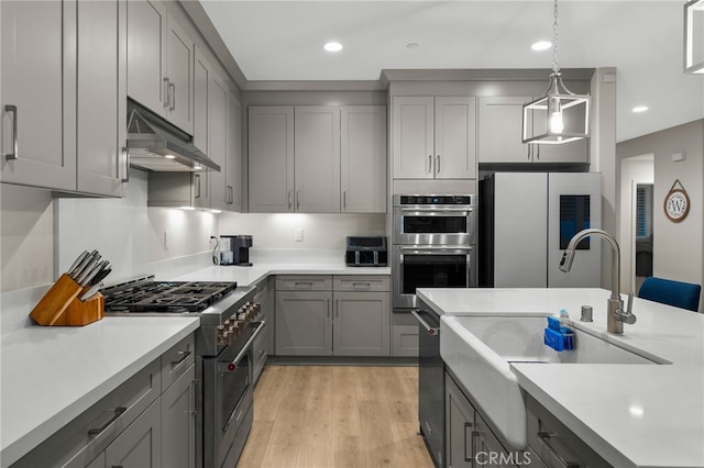 kitchen featuring appliances with stainless steel finishes, light countertops, gray cabinets, decorative light fixtures, and under cabinet range hood