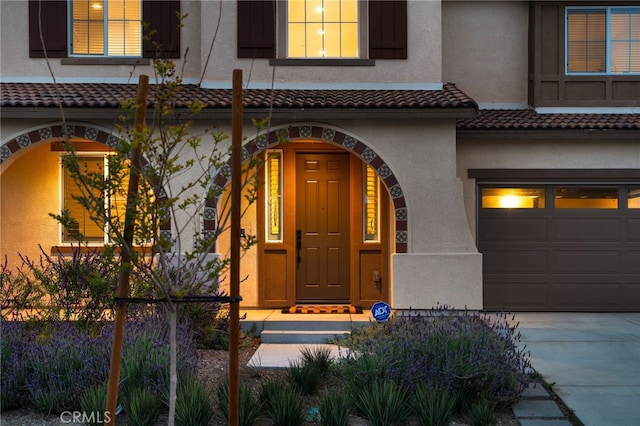 property entrance featuring an attached garage, stucco siding, driveway, and fence