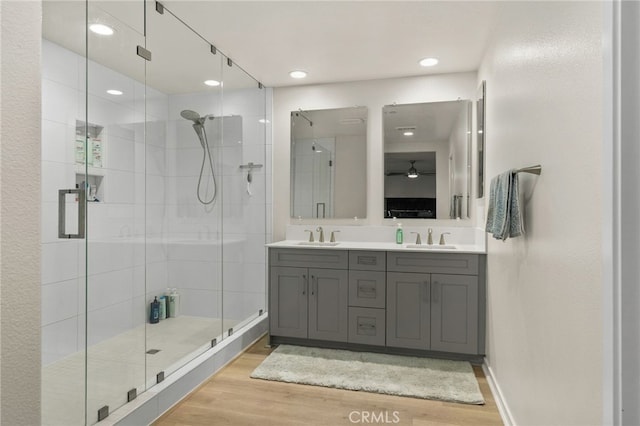 bathroom with double vanity, a shower stall, wood finished floors, a sink, and recessed lighting