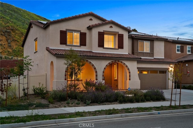 mediterranean / spanish-style house featuring fence, stucco siding, a tiled roof, concrete driveway, and an attached garage