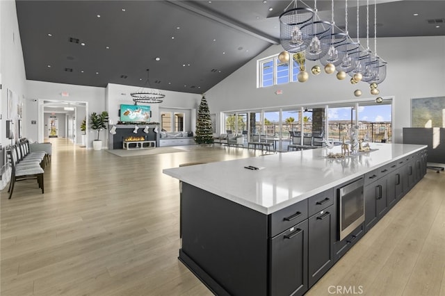 kitchen with light countertops, high vaulted ceiling, stainless steel microwave, light wood-type flooring, and a spacious island