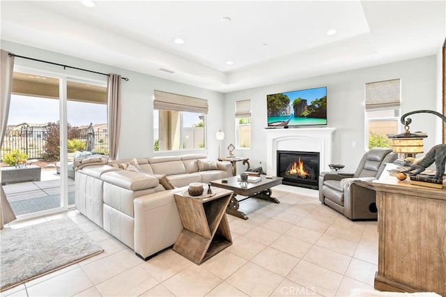 living area featuring a glass covered fireplace, a healthy amount of sunlight, light tile patterned floors, and a raised ceiling