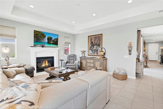 living area with light tile patterned floors, a glass covered fireplace, recessed lighting, and a tray ceiling
