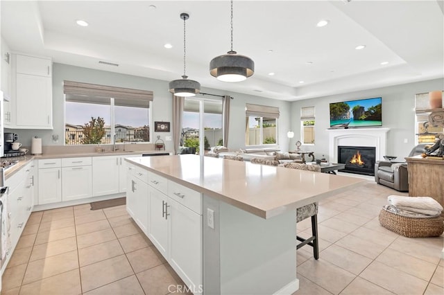 kitchen featuring light tile patterned flooring, open floor plan, a kitchen breakfast bar, a lit fireplace, and a tray ceiling