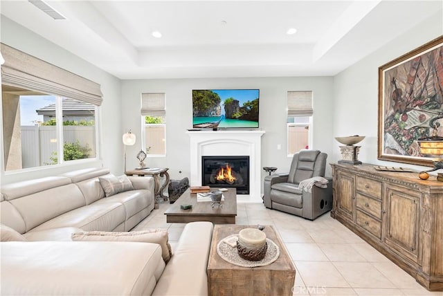 living area with a glass covered fireplace, a raised ceiling, light tile patterned flooring, and visible vents