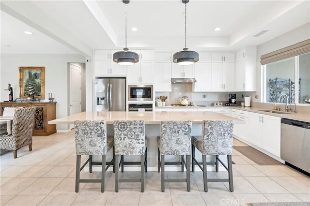 kitchen with appliances with stainless steel finishes, a sink, light countertops, a kitchen island, and under cabinet range hood