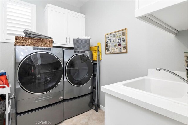 clothes washing area featuring light tile patterned floors, independent washer and dryer, cabinet space, and a sink
