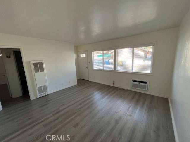 unfurnished living room with baseboards, a wall mounted air conditioner, wood finished floors, and a heating unit