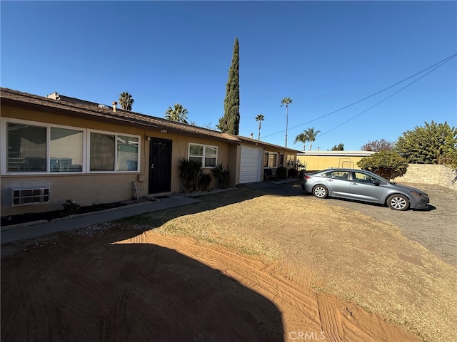 ranch-style house with a garage, dirt driveway, and stucco siding