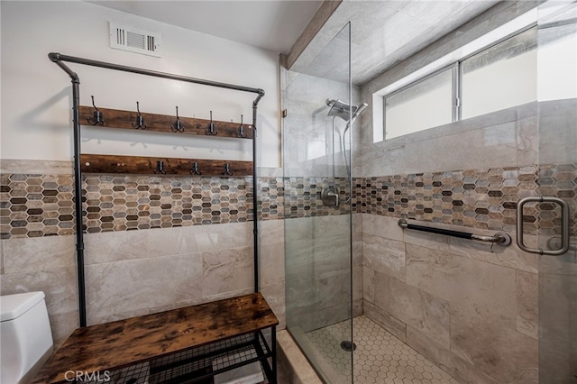 bathroom with toilet, visible vents, a shower stall, and tile walls