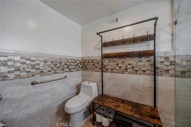 bathroom featuring visible vents, toilet, tile walls, a wainscoted wall, and a tile shower