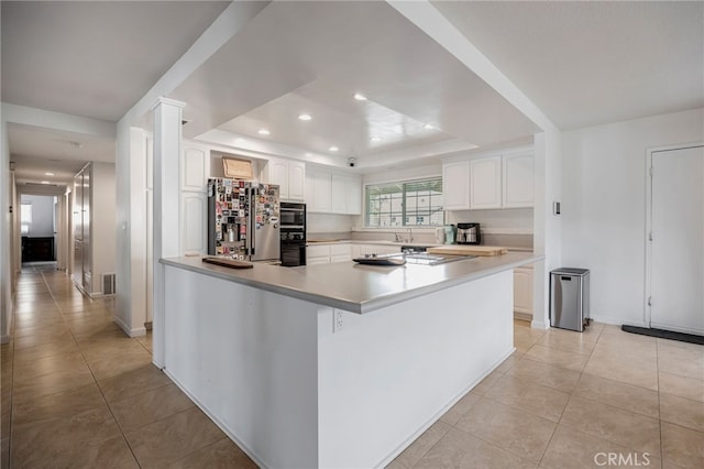 kitchen featuring light tile patterned floors, a raised ceiling, white cabinets, light countertops, and black appliances