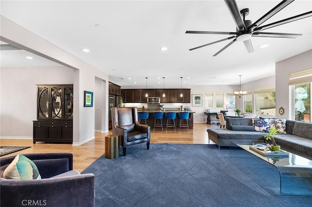 living area featuring recessed lighting, baseboards, ceiling fan with notable chandelier, and light wood-style floors