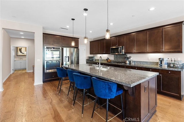 kitchen with a sink, light wood-style flooring, dark brown cabinets, and stainless steel appliances