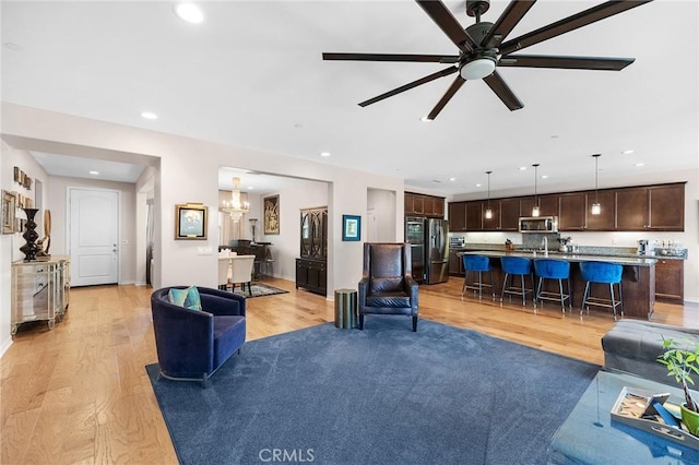 living room featuring light wood-type flooring, recessed lighting, baseboards, and ceiling fan with notable chandelier
