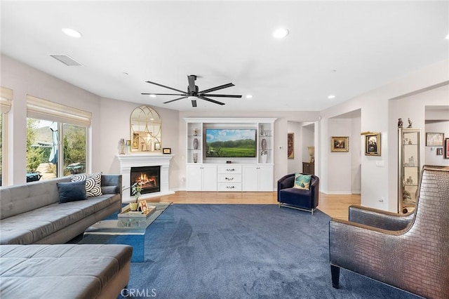 living room with a warm lit fireplace, ceiling fan, light wood finished floors, recessed lighting, and visible vents