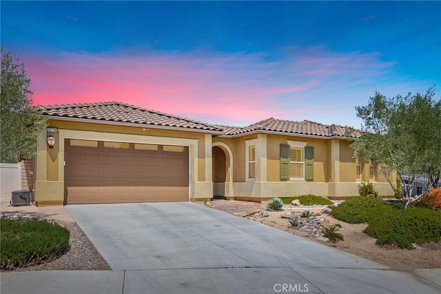mediterranean / spanish-style house with an attached garage, stucco siding, a tile roof, and concrete driveway