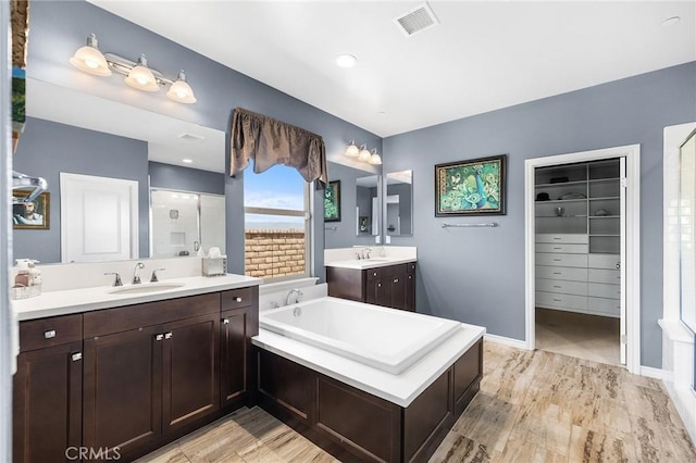 bathroom with visible vents, a garden tub, two vanities, a sink, and a stall shower