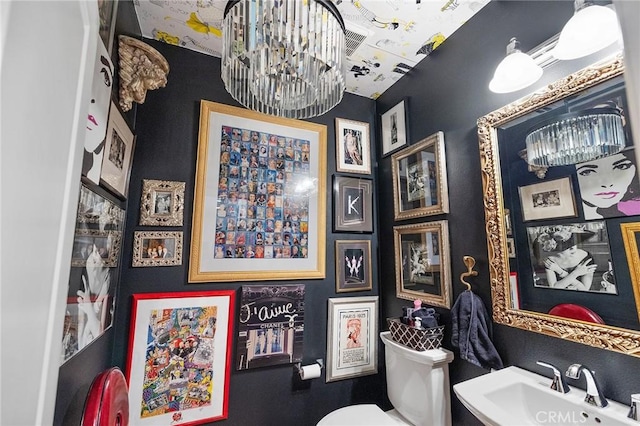 half bath featuring toilet, a chandelier, and a sink