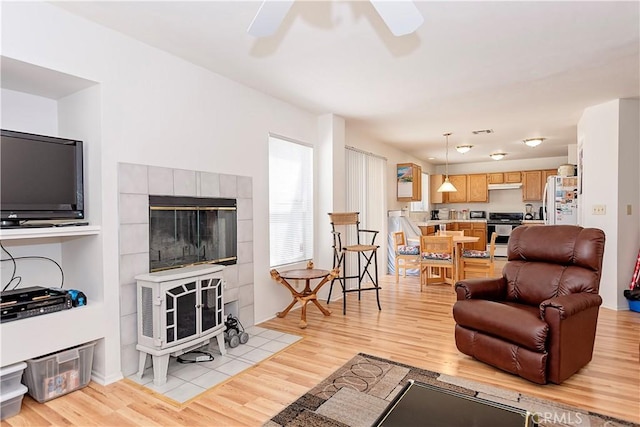 living room featuring a wood stove, light wood finished floors, and ceiling fan