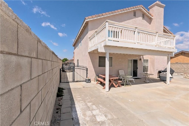 back of house with fence, a balcony, stucco siding, a gate, and a patio area