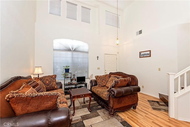living room featuring visible vents, light wood-type flooring, baseboards, a high ceiling, and stairs