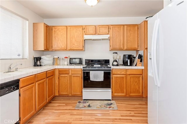 kitchen with a sink, light wood-type flooring, under cabinet range hood, and white appliances