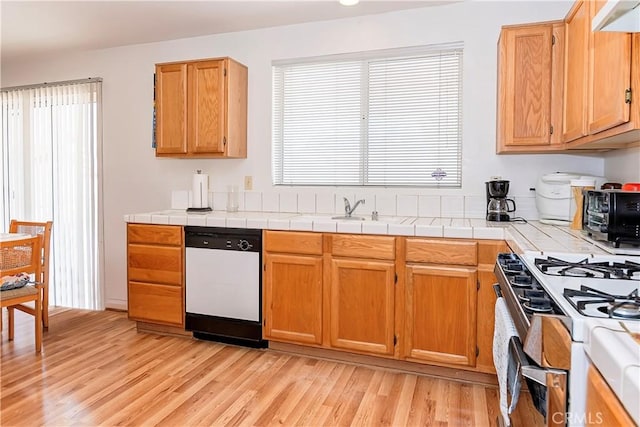 kitchen with a sink, a toaster, light wood finished floors, tile counters, and white appliances