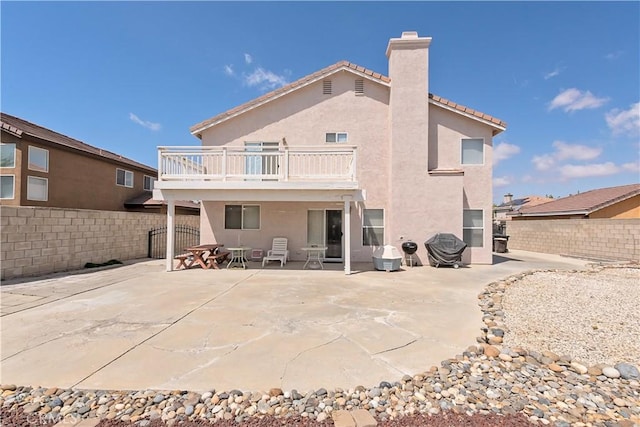 back of house featuring a chimney, a balcony, a fenced backyard, and stucco siding