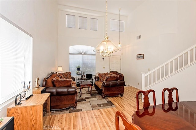 living room featuring visible vents, an inviting chandelier, a towering ceiling, light wood-style floors, and stairway