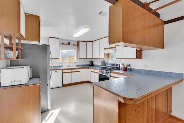 kitchen with visible vents, a peninsula, white appliances, under cabinet range hood, and a sink