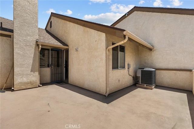 rear view of house featuring a patio, central AC, stucco siding, and a chimney