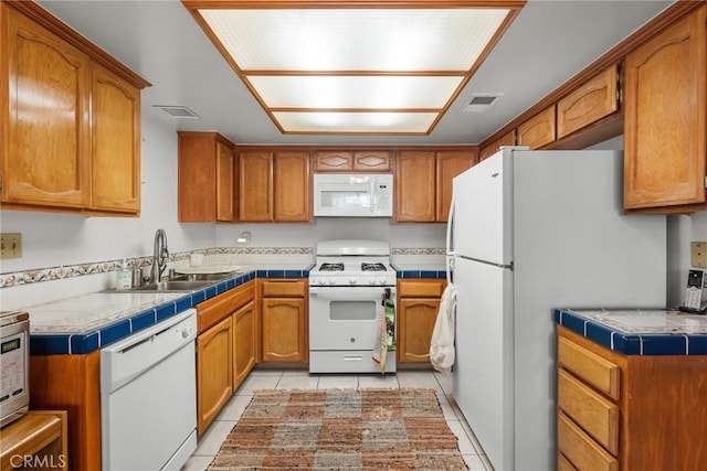 kitchen featuring a sink, brown cabinets, white appliances, and light tile patterned flooring