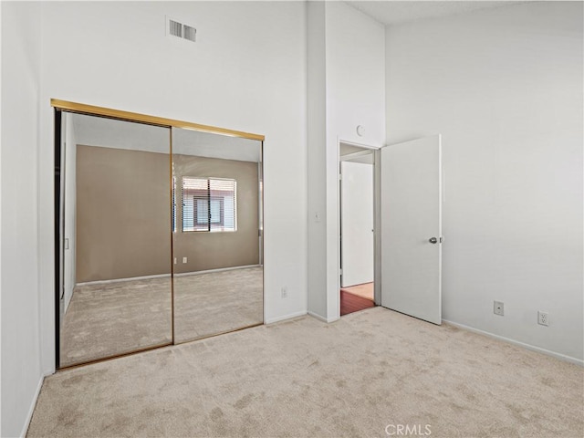 unfurnished bedroom featuring a towering ceiling, visible vents, baseboards, a closet, and carpet flooring