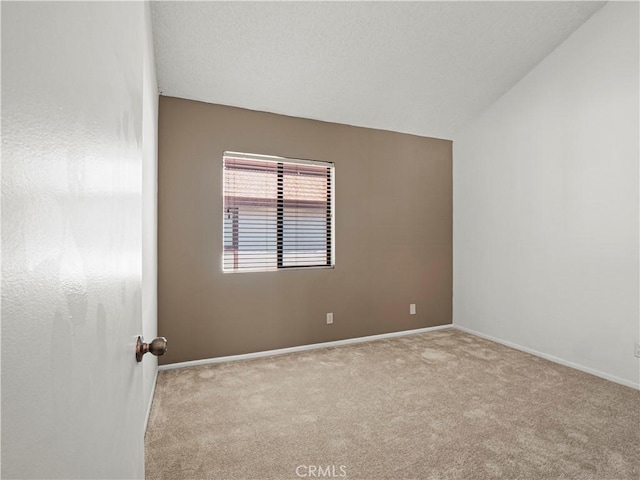 empty room featuring carpet floors, baseboards, and vaulted ceiling