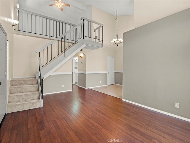 unfurnished living room featuring ceiling fan with notable chandelier, stairs, baseboards, wood finished floors, and a towering ceiling