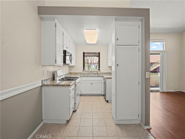 kitchen with white gas range, a sink, light stone counters, white cabinets, and stainless steel microwave