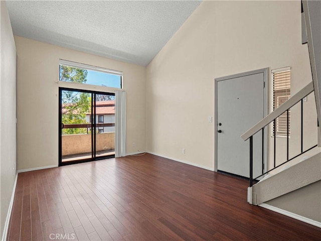 spare room with a textured ceiling, high vaulted ceiling, baseboards, wood finished floors, and stairway