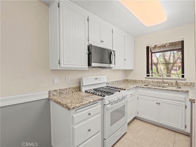 kitchen featuring light stone counters, a sink, gas range gas stove, white cabinetry, and stainless steel microwave