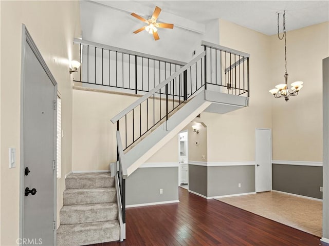 stairway featuring baseboards, ceiling fan with notable chandelier, wood finished floors, and a towering ceiling