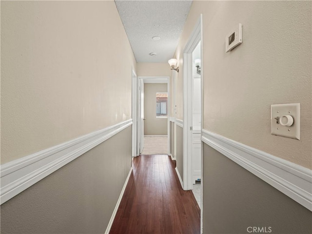 hallway with baseboards, a textured ceiling, and dark wood-style flooring